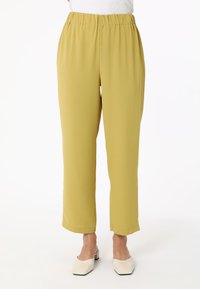 Gelbe, elastische Hosen mit geradem Schnitt und weitem Bein. Glatte Textur, ohne Muster. Getragen mit hellen, blockabsatzschuhen.