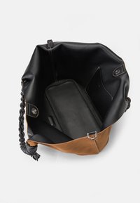 Bolsa tote de couro com um design em duas cores, sendo a parte superior preta e a inferior castanha. O interior possui uma textura suave e um bolso para organização.