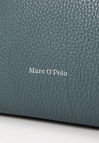 Tyrkysová kožená textura s jemným zrnom. Obsahuje embosované logo "Marc O'Polo" v bielej farbe, umiestnené výrazne na povrchu.