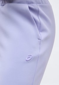 Αθλητικό παντελόνι σε ανοιχτό μωβ χρώμα με ελαστική μέση, πλαϊνή τσέπη και ανάγλυφο μινιμαλιστικό λογότυπο κοντά στην τσέπη.