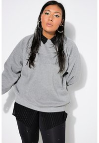 Felpa grigia oversize con colletto nero, caratterizzata da un logo sottile. Abbinata a pantaloni corti neri a righe e leggings con dettagli.