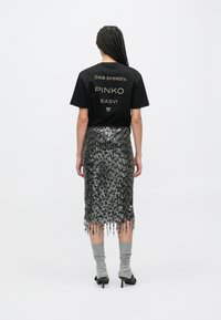 Črna majica s kratkimi rokavi z zlato napisom na hrbtu, kombinirana s srebrno svinčeno krilo s cofki iz bleščic. Sive nogavice do kolen in črni čevlji s peto.