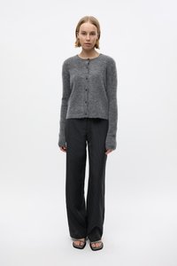 Gray knitted cardigan with a round neckline and five buttons, paired with black vertical striped trousers. Model stands in a neutral background.