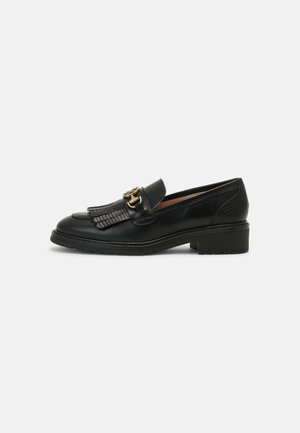 Mocassin en cuir noir avec petit talon bloc, détail en franges à l'avant et boucle métallisée dorée sur le dessus.