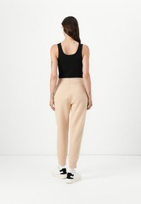 Svart åtsittande linne med breda axelband ihop med beige joggers med sidodekorer, ribbade manschetter och vita sneakers med svarta accenter.