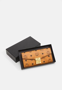Billetera marrón con patrón de logo MCM en negro, superficie texturizada, cierre de gancho dorado, colocada en una caja negra.