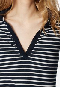Hlavní modro-bílý pruhovaný top s výstřihem do V. Vyroben z žebrované tkaniny, má přiléhavý střih a kontrastní lemování kolem výstřihu.