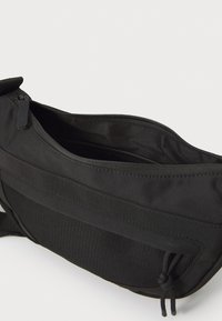 Schwarze, rechteckige Tasche aus strapazierfähigem Stoff mit einem Reißverschluss oben. Verfügt über ein strukturiertes Netzpaneel und einen verstellbaren Tragegurt für Vielseitigkeit.