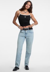 Top corto negro sin mangas con ribete blanco y detalle de estrella plateada, combinado con jeans rectos de un tono azul claro. Modelo lleva un cinturón negro y zapatos.