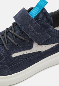 Navy blue sneaker with suede upper, mesh accents, and a grey design element. It features a Velcro strap and flat laces, with a white sole.