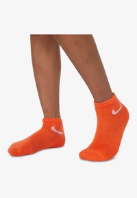 Narancssárga crew zoknik lélegző szövetből, bordás textúrával, az oldalukon egy fehér Nike logóval.