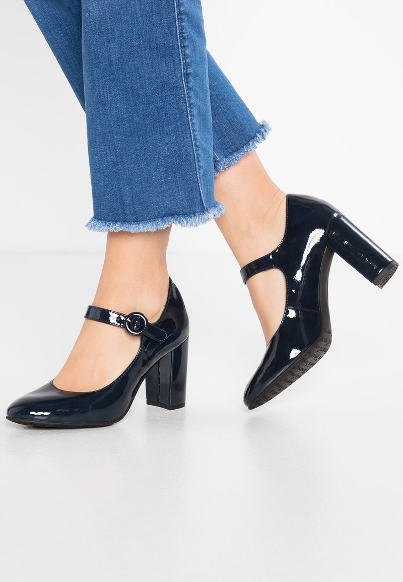 Escarpins en cuir verni marine avec un bout rond, une bride de cheville avec une boucle ronde et un talon épais. Pantalon en denim avec ourlet effiloché.