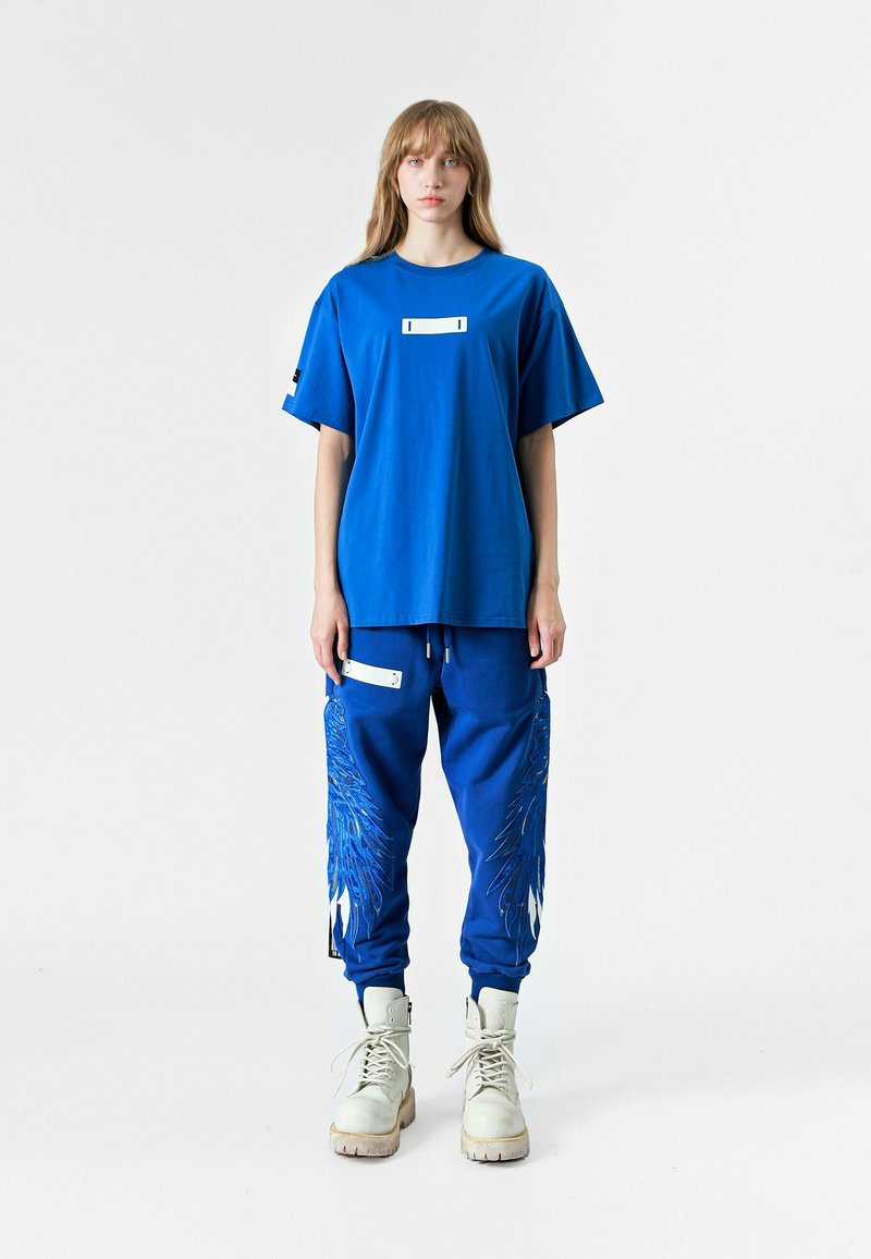 Camiseta de algodón azul de manga corta con un parche rectangular en el pecho. Los joggers azules a juego cuentan con bordados de plumas blancas y bolsillos.