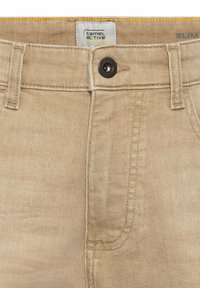 Jean slim beige en denim avec une texture lisse, doté d'un bouton noir, de coutures contrastantes et d'une étiquette portant la mention "camel active."