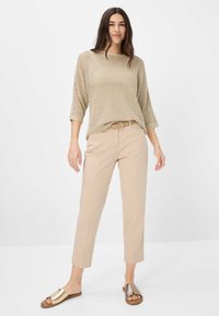 Beige gebreid sweater met een losse pasvorm en open weefsel, gecombineerd met beige op maat gemaakte broeken en metallic slip-on sandalen.