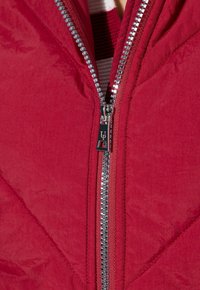 Chaqueta acolchada roja con textura de acolchado, presenta una cremallera plateada y un tirador de marca en el cuello.