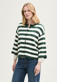 Gestreifter Cardigan in Dunkelgrün und Weiß, mit rundem Halsausschnitt, Knöpfen und weiten Ärmeln, getragen über blauen Jeans.