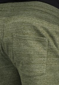 Grüne, strukturierte Jogginghosen mit einem gerippten Bund und einer Gesäßtasche. Der Stoff hat ein meliertes Muster und eine weiche Oberfläche.