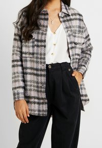 Plaid oversized shirt jacket in soft, textured fabric with hues of lavender, black, and gray. Features metal buttons and a buttoned front.