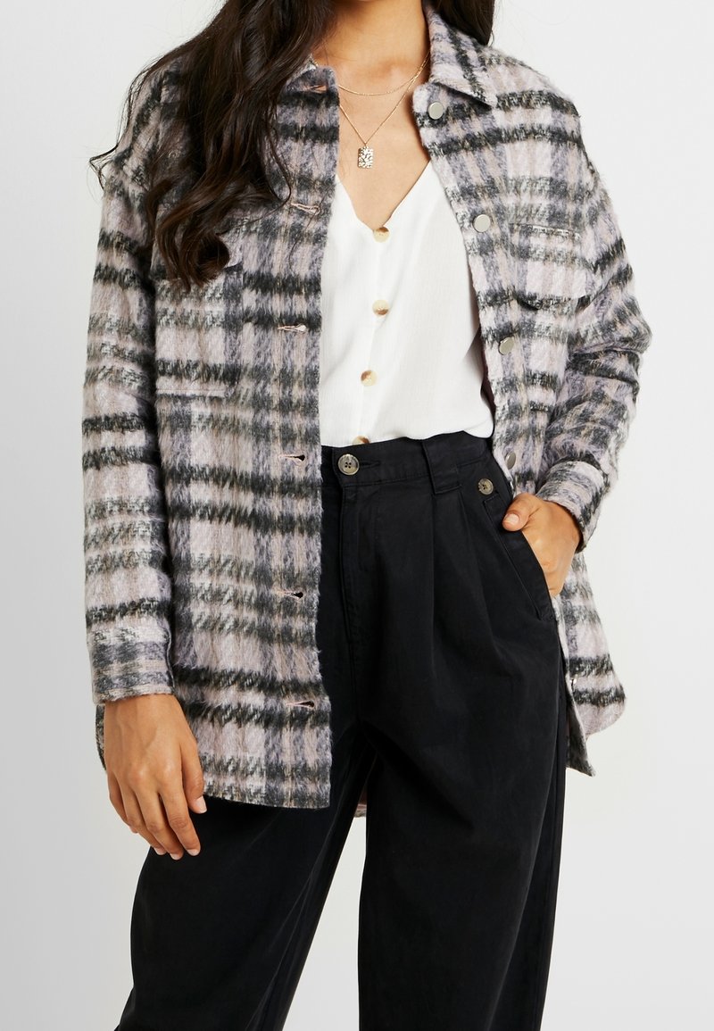 Plaid oversized shirt jacket in soft, textured fabric with hues of lavender, black, and gray. Features metal buttons and a buttoned front.
