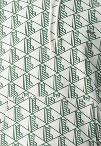 Felpa con cappuccio caratterizzata da un motivo geometrico in verde e bianco. Presenta una tasca a marsupio e un piccolo logo del marchio sul petto.