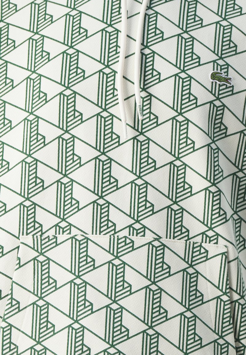 Sudadera con capucha con un patrón geométrico en verde y blanco. Cuenta con un bolsillo tipo canguro y un pequeño logo de la marca en el pecho.