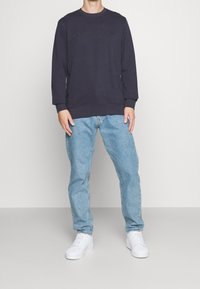 Sudadera azul marino con texto en relieve "COPENHAGUE", combinada con jeans azul claro y zapatillas blancas. Diseño sencillo y casual.