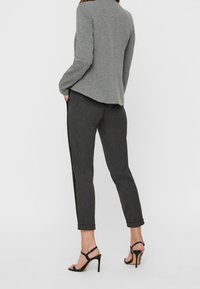 Grå fitted blazer med en struktureret skæring, parret med mørke, let skræddersyede bukser. Sorte sandaletter med stropper og høje hæle fuldender looket.