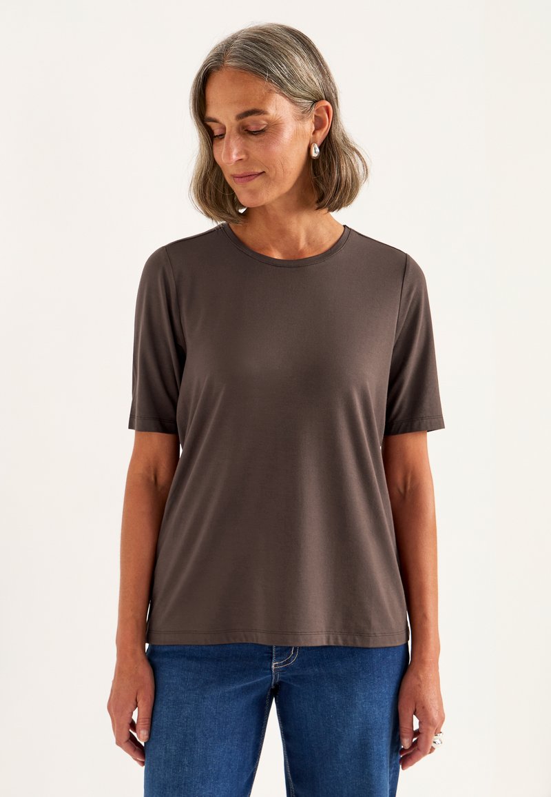Brun kortærmet t-shirt i et blødt, glat stof med rund hals, parret med blå denimjeans. Enkel, løs pasform.