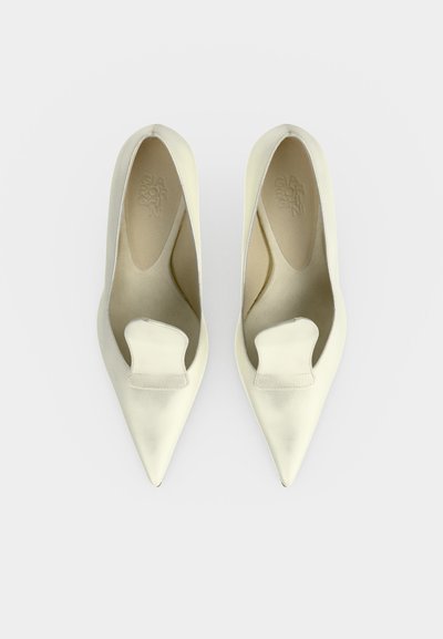 Ζευγάρι κρεμ μπαλαρίνες από δέρμα με μυτερή μύτη και μια χαρακτηριστική διπλωμένη δερμάτινη λεπτομέρεια στην κορυφή, φωτογραφημένες από ψηλά σε λευκό φόντο.