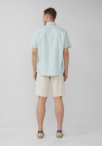 Korte mouwen geblokte overhemd in lichtblauw en wit, gecombineerd met crèmekleurige shorts en tan schoenen. Het overhemd heeft een button-down kraag en een achterpaneel.