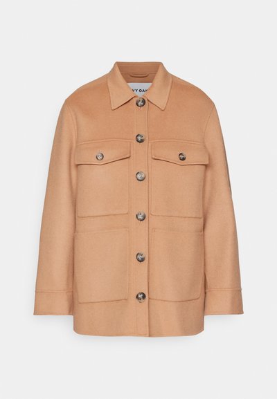 Giacca in misto lana color sabbia con colletto, chiusura con bottoni frontali e due tasche sul petto. Presenta bottoni grandi e una vestibilità leggermente sagomata.