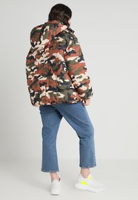 Kamo raštas pūkinė striukė su žemiškais žalių, rudų ir smėlio atspalviais. Didelė kapšą ir dekoratyvinė siuvinėta tekstūra. Derinama su trumpais džinsais.