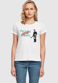 Hvid bomulds-t-shirt med grøn tekst, der siger "FØLG DINE DRØMME" med "AFVIST" i rødt, sammen med en sort-hvid grafik af en mand.