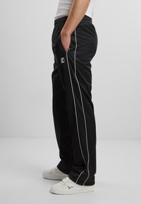 Pantaloni sport negri cu dungi albe pe laterale, talie elastică și buzunare laterale, asortați cu adidași albi și un tricou alb ajustat.