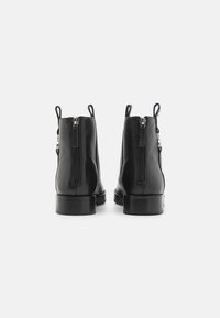 Sorte lærreim ankle boots med en glatt tekstur, bakzipper og løftestropper, med en solid blokkhelt og minimalistisk design.