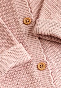 Helle rosa Strickjacke mit gerippten Bündchen und Saum, ausgestattet mit Holzknöpfen und einem strukturierten Muster auf dem Stoff.