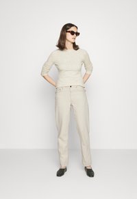 Bež pleteni pulover i svijetlosmeđe hlače opuštenog kroja. Tamne sunčane naočale i crni klompe upotpunjuju outfit.