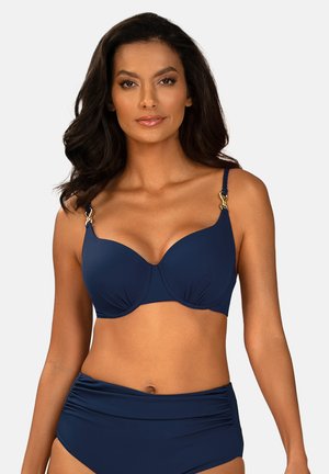 Kobieta o długich ciemnych włosach, ubrana w granatowy bikini z ramiączkami ozdobionymi złotymi akcentami, na jednolitym jasnym tle.