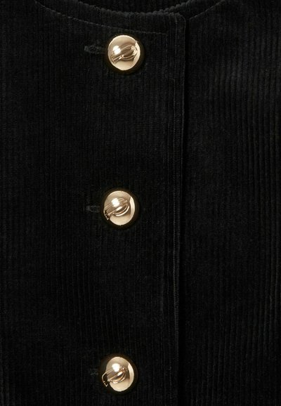 Tessuto di velluto a coste nero con righe verticali, caratterizzato da tre grandi bottoni rotondi dorati sul davanti, che aggiungono un accento metallico.