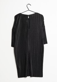 Svart klänning med ett strukturerat mönster, långa ärmar och en nyckelhålsdetalj baktill, hängande på en svart krok mot en vit bakgrund.