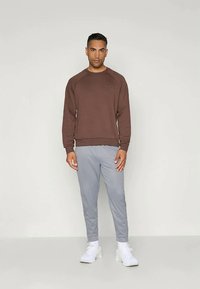 Brūns džemperis ar ribotu apakšmalu un aprocēm, kombinēts ar gaiši pelēkiem šauriem joggeriem. Balti sporta apavi noslēdz apģērbu.