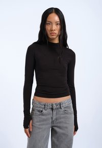 Black long-sleeve top in a fitted design with soft fabric, paired with light gray high-waisted jeans featuring front pockets and a button closure.