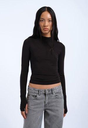 Black long-sleeve top in a fitted design with soft fabric, paired with light gray high-waisted jeans featuring front pockets and a button closure.