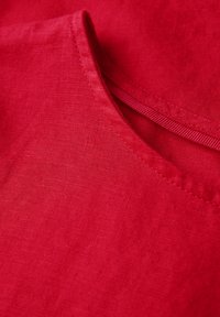 Tessuto di lino rosso con una superficie liscia, dotato di un collo rotondo e di un piccolo dettaglio a tasca.