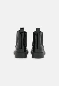 Botas de tobillo de charol negro con paneles laterales elásticos, tiradores y suelas de goma texturizada, con un acabado suave y brillante.