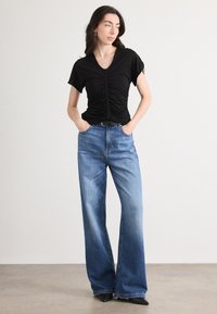 Black ruched t-shirt with v-neck, paired with light blue wide-leg jeans featuring a faded gradient effect and a black belt accent.
