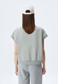 Laatikkomallinen harmaa lyhyt hiha sweatshirt, pehmeä pinta ja ribattu helma, yhdistettynä vaaleanharmaisiin collegehousuihin ja valkoiseen lippalakkiin.