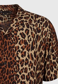 Camisa de manga corta en tejido ligero con un estampado de leopardo en tonos de marrón sobre un fondo beige, y un solo botón negro.