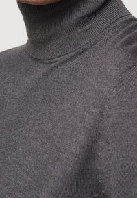 Pull à col roulé gris en tissu tricoté côtelé, doté d'un col près du cou et de détails d'épaule sans coutures, avec une texture subtile.